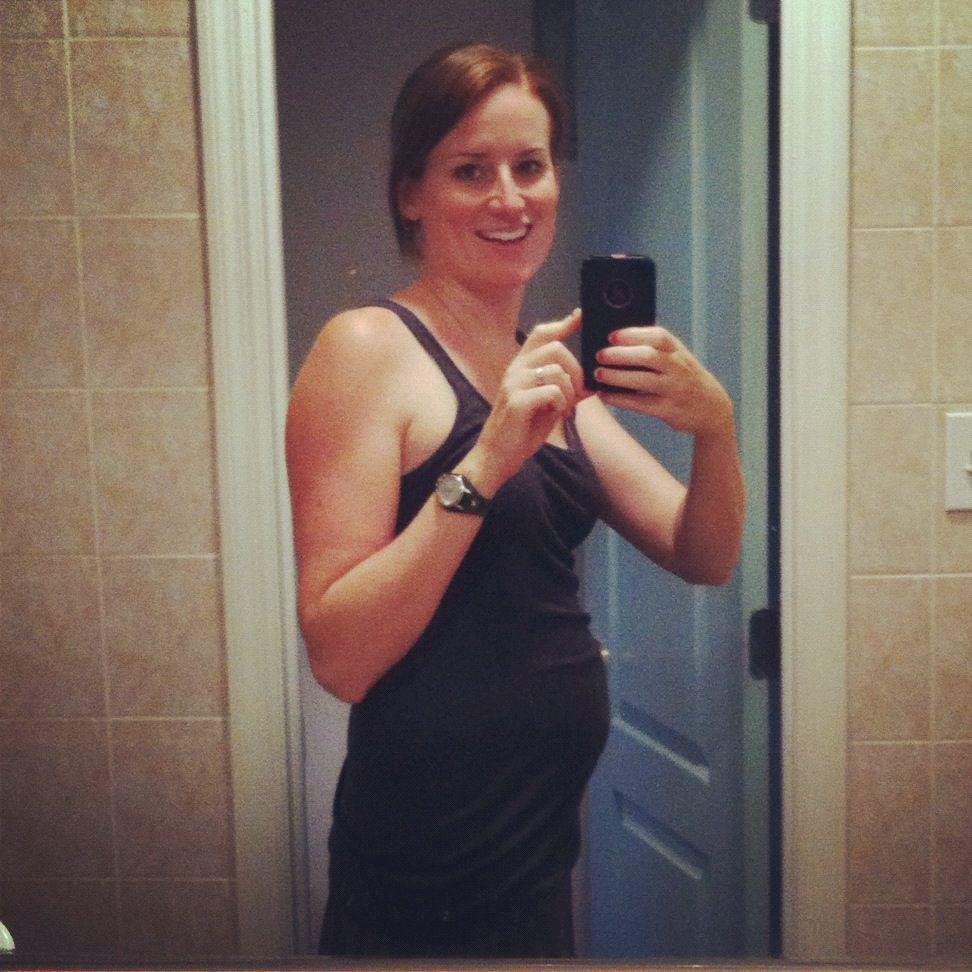 woman in brown tank top taking selfie in mirror for 14 weeks pregnant belly photo