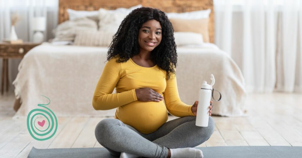 black pregnant woman with yellow shirt sitting on a yoga mat with a water bottle